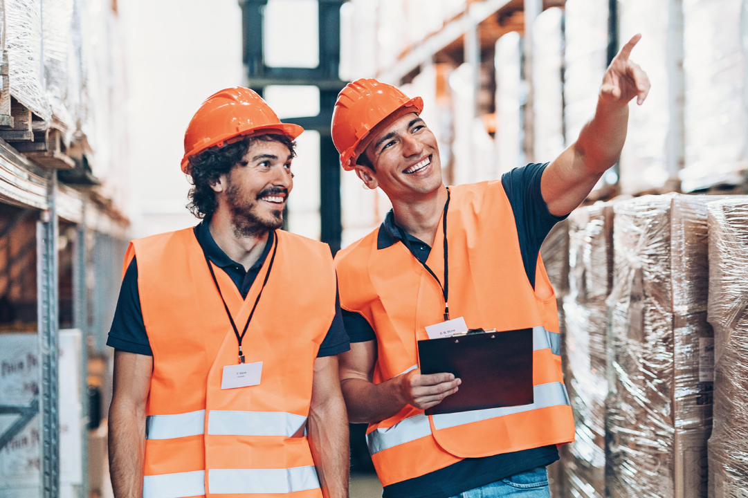 Two warehouse workers smiling, wearing hi-vis vests and helmets